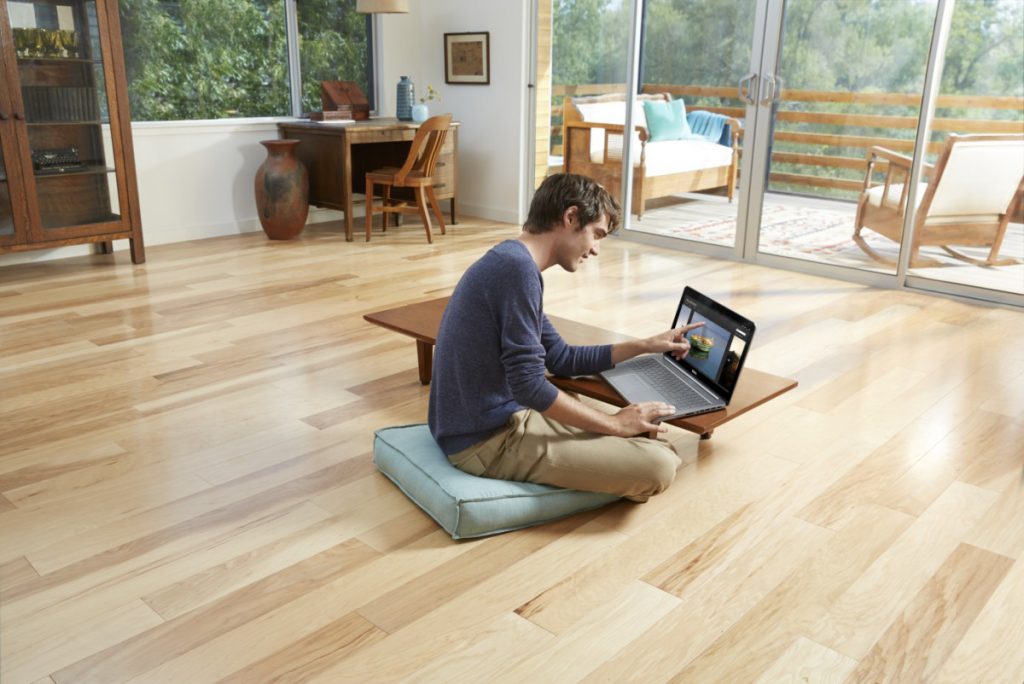Man using Dell Inspiron 15 (7537) Touch notebook computer seated on a floor cushion at a low coffee table in a minimalist living room.